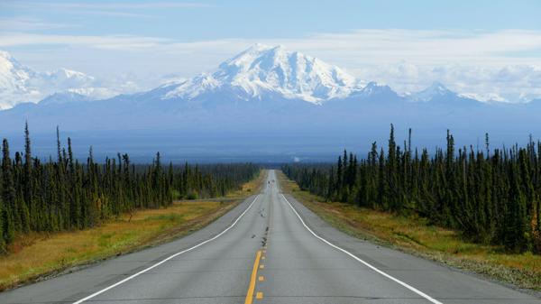 Glenn Highway stretches into the center of the photo with Mount Drum in the background, Spruce trees surround the highway.